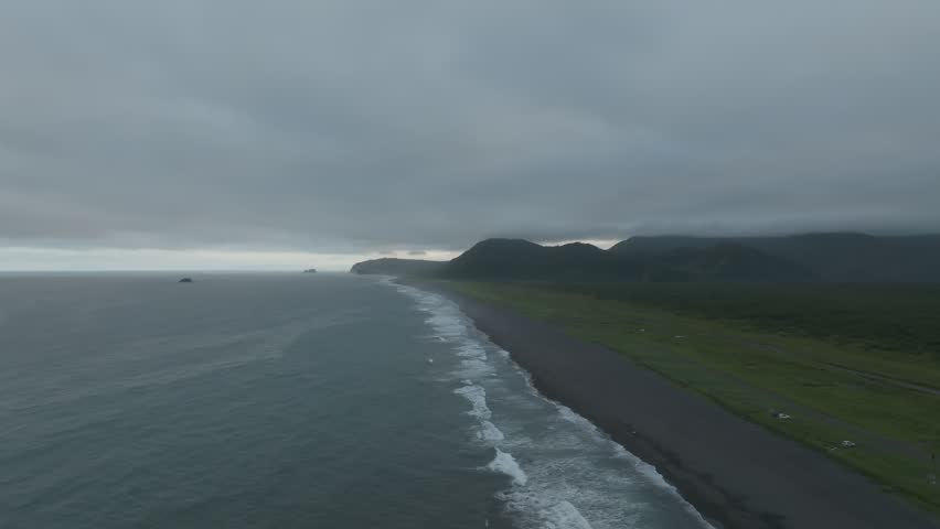 Drone footage of Khalaktyrsky Beach with black volcanic sand, ocean waves and moody cloudy sky along the Pacific coast of Kamchatka Krai, Russia