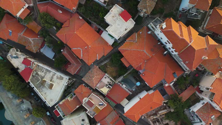 An aerial top-down drone shot captures the stone walls of the medieval Kavala Fortress and the traditional rooftops of Panagia Old Town. The scene is illuminated by bright morning sunlight over the coastal city in Greece.