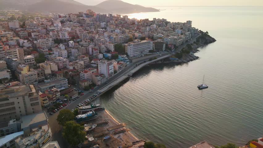 High-angle drone sweep across the red-tiled roofs and dense urban architecture of Kavala at sunrise, overlooking the Aegean Sea and Thracian coastline.