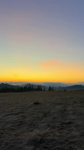 A beautiful sunrise lights up the sky with orange hues. The sun rises above the hills and clouds, creating a colorful morning in the Carpathian mountains.