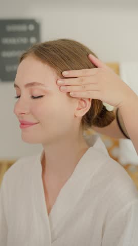 Beautiful woman getting head and facial massage treatment at beauty spa. Attractive girl sitting on massage bed, getting relaxing physiotherapy service from masseuse for body care in luxury spa clinic