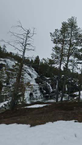Cinematic Vertical FPV over icy waterfall stream in snowy alpine wilderness
