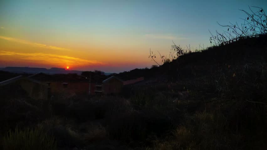 scenic dawn landscape with glowing sun rising above distant mountain horizon