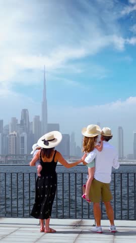 A tourist family standing at the Creek looks at the urban skyline of Dubai, UAE, during their city vacations