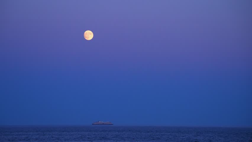 Full moon and cruise ship gliding over Atlantic Ocean from beach in Acadia National Park, Maine.