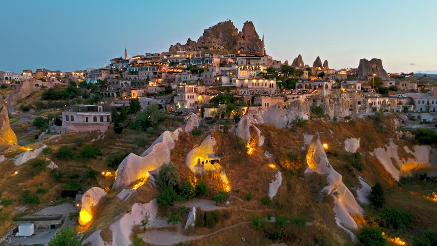 Drone view of Uchisar at night, Cappadocia, Turkey. Illuminated streets, cave homes and Uchisar Castle give a dramatic evening view.