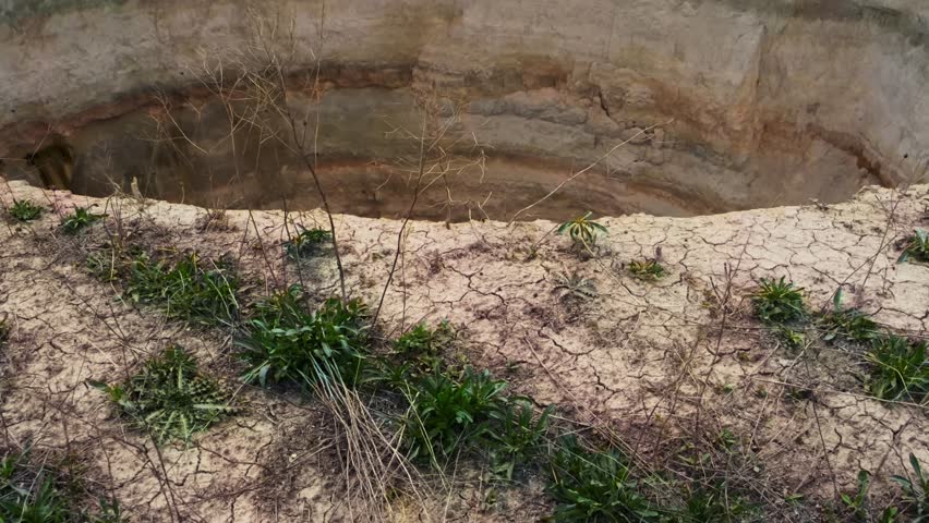 Ground-level footage showing a large sinkhole with steep eroded walls in a rural landscape. Geological formation, natural ground collapse, karst terrain, and dry soil textures are clearly visible.