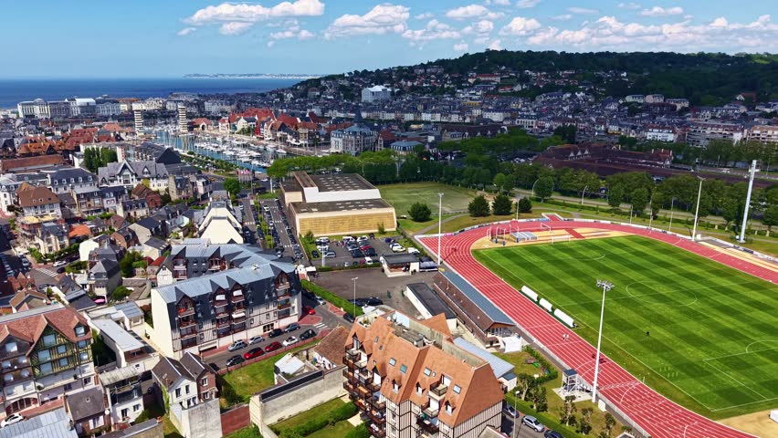 Athletics track and field stadium surrounded by traditional architecture of Deauville, Normandy, France. Aerial backward