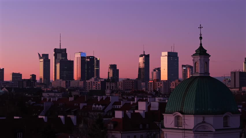 Cinematic aerial view of Warsaw city center during purple sunset. Transition from historical architecture to modern glass skyscrapers. Dynamic camera movement across urban cityscape at dusk.