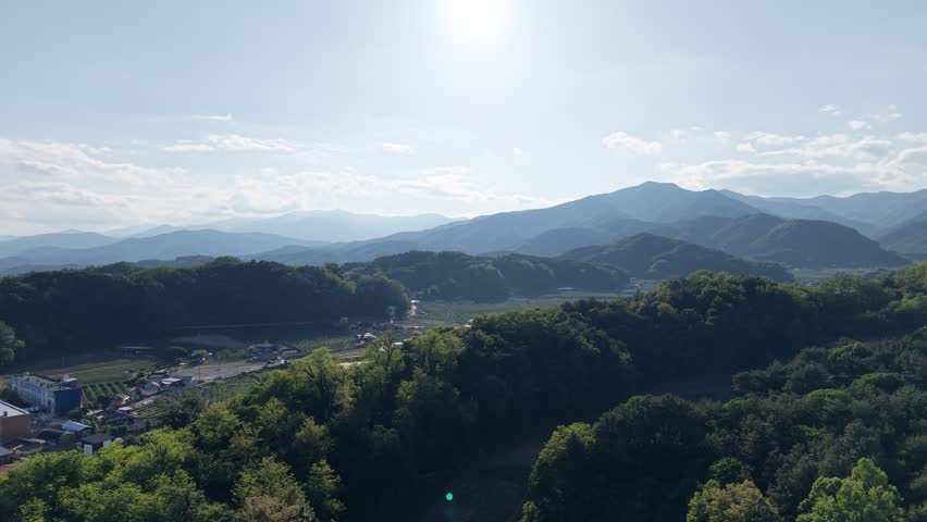 Aerial drone shot of a peaceful countryside village nestled under the majestic Sobaeksan mountain ridges in Yeongju, South Korea. 4K resolution.