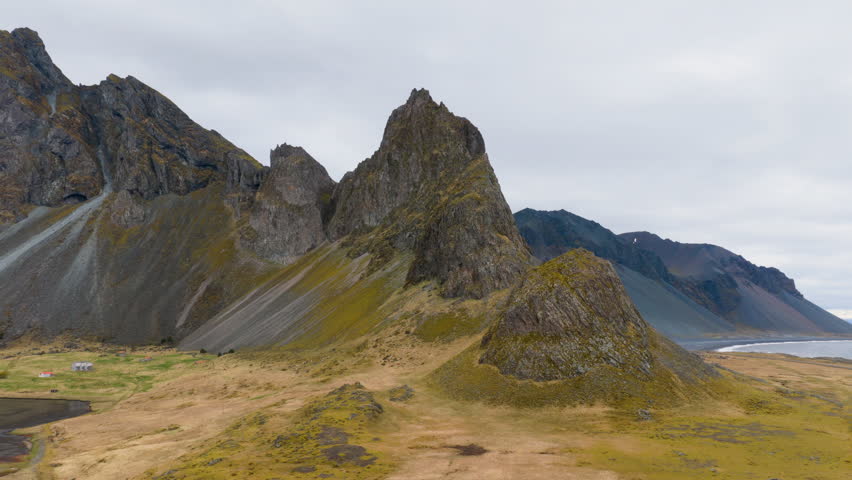 Jagged mountain peak above rugged coastal cliffs with calm water under an overcast sky. Iceland