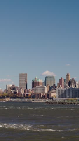 Waterfront view of Manhattan cityscape with modern and historic architecture, blue sky and waves.