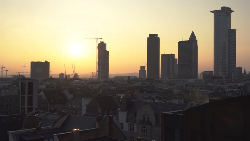 Dynamic sunrise footage over Frankfurt city skyline, tall modern skyscrapers and construction site, dawn light illuminates cityscape, urban view.