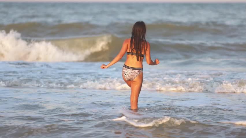 A girl with loose hair walks on the sea with waves and enjoys the sun