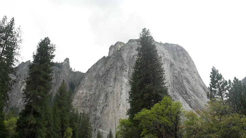 Majestic granite monolith of el capitan towering above the lush green forest and reflecting in the calm waters of the merced river on a cloudy day in yosemite valley, california