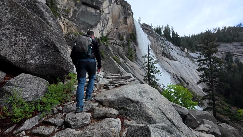 Male hiker with a backpack walking down the stone stairs of the mist trail, a scenic path leading to vernal and nevada falls in yosemite national park, california, on a cloudy summer day