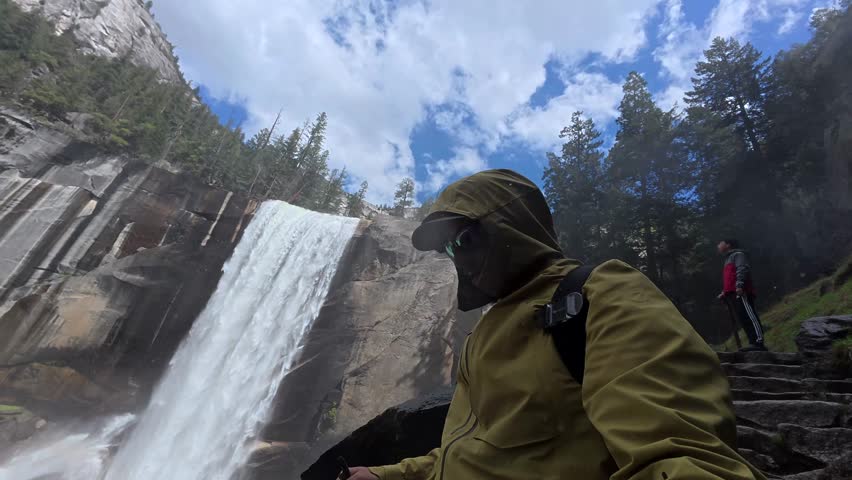 Point of view shot of a young man wearing a waterproof jacket while hiking on the stone steps of the wet and slippery mist trail near the majestic vernal fall in yosemite national park, california