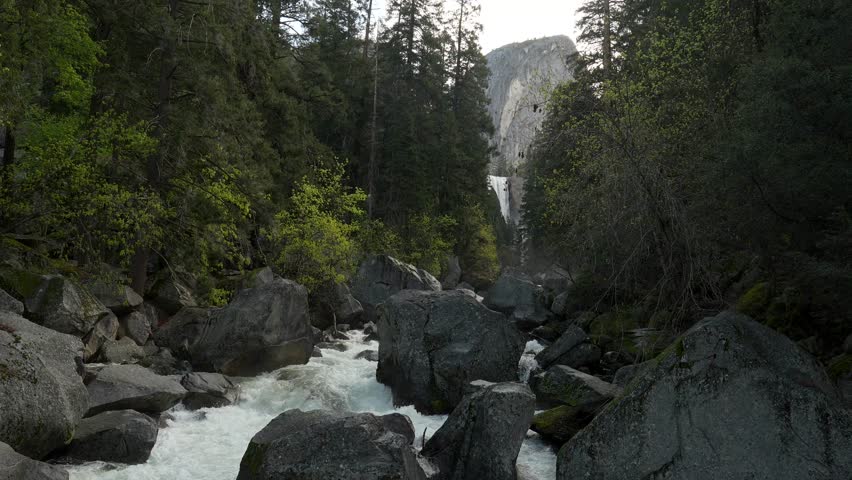 Majestic view of the merced river cascading over large granite boulders along the mist trail, with the powerful vernal fall visible in the distance within yosemite national park, california
