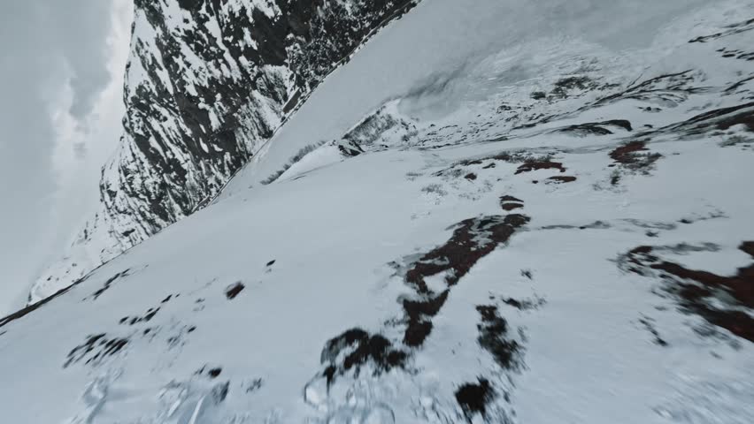 Fast FPV drone diving down a mountain ridge towards a frozen lake in Nordic valley landscape