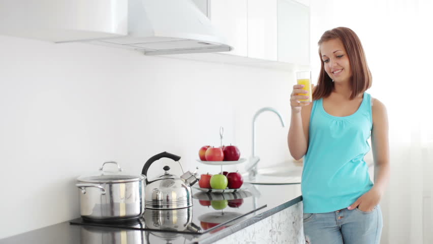 Girl standing in kitchen and holding glass of orange juice

