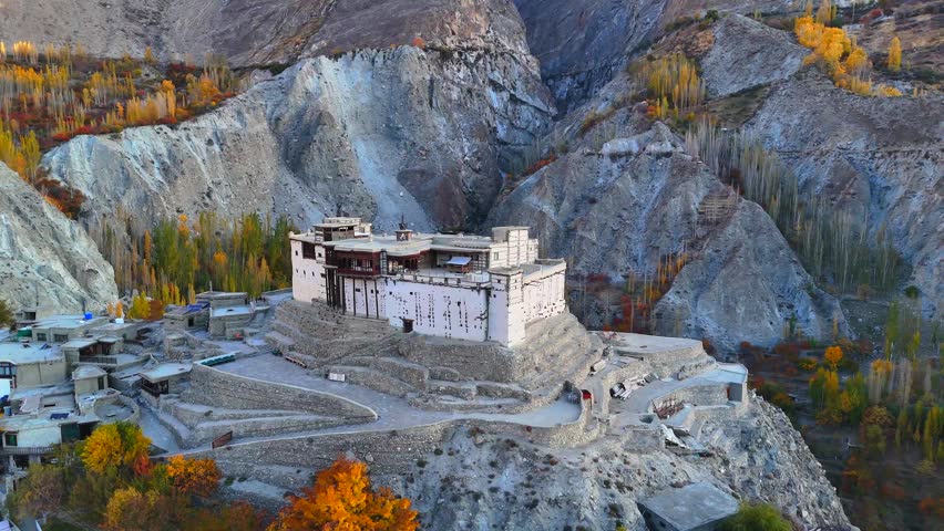 Aerial view of the historic Baltit Fort perched on a hill surrounded by rugged mountains and autumn foliage in Karimabad, Gilgit Baltistan, Pakistan.