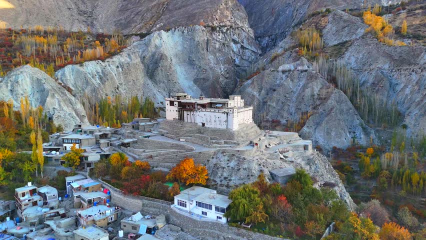 Aerial view of the historic Baltit Fort perched on a hill surrounded by vibrant autumn foliage and the rugged mountains of the Hunza Valley in Karimabad, Gilgit Baltistan, Pakistan.
