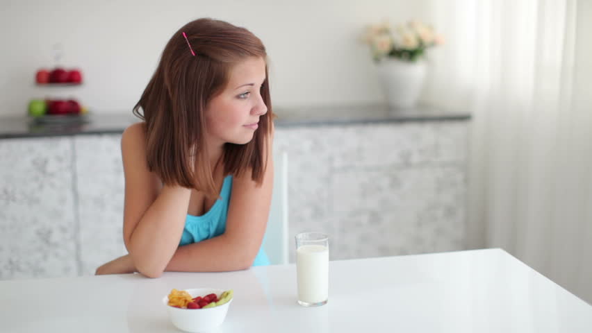 Girl sitting at table and in front of her  is glass of milk and fruit in bowl
