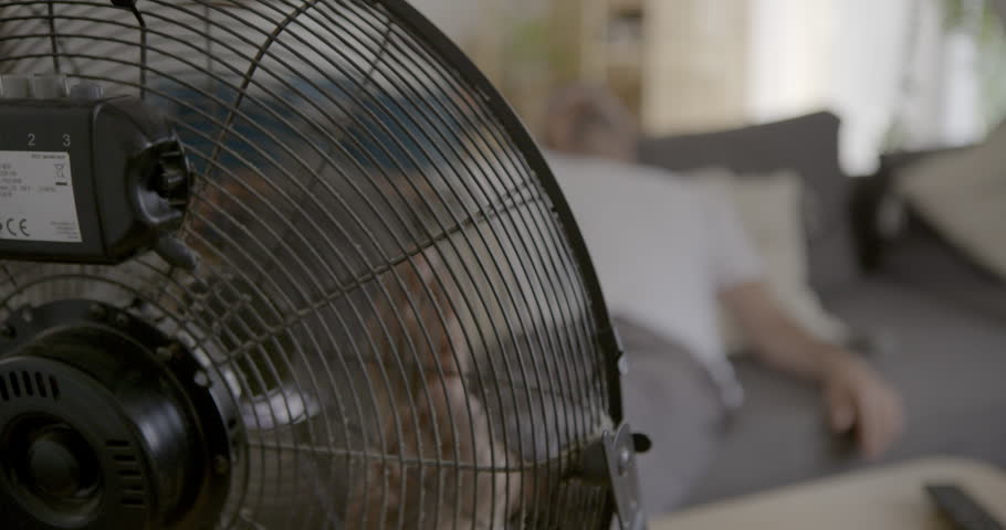  Cooling Breeze: A powerful electric fan circulates air, providing a welcome respite from the heat for a person relaxing on a sofa.

