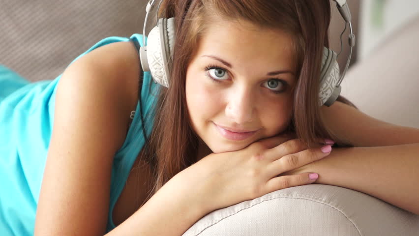 Girl lying on sofa and listening music with smile
