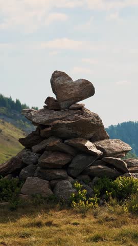Traditional stone cairn trail marker standing on alpine meadow under blue sky with fluffy clouds. Symbol of mountain hiking and navigation in the Alps.