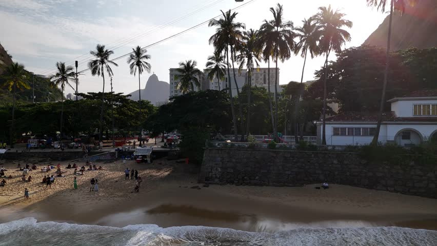 Aerial view of Praia Vermelha with palm trees, people on the sand and Christ the Redeemer in the background, Rio de Janeiro, State of Rio de Janeiro, Brazil.