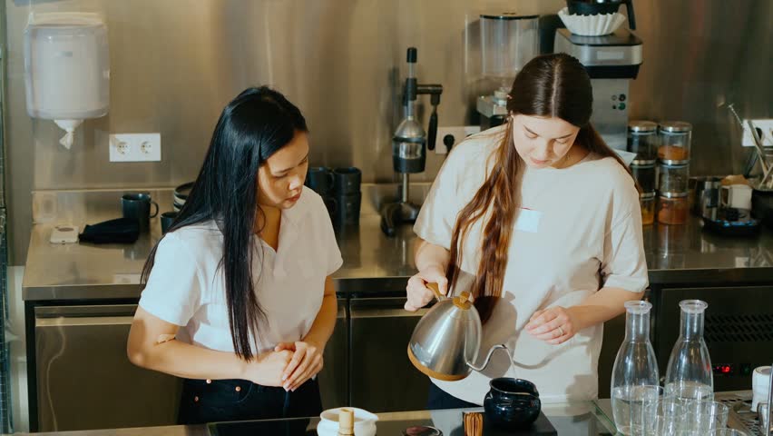 A female barista and a female intern are pouring from a kettle into a jug
