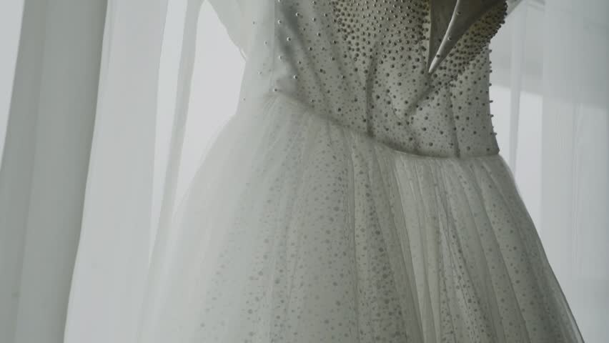 A white wedding dress hangs on the window
