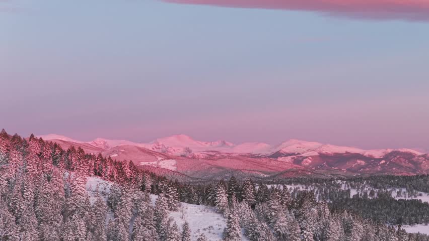 Vibrant alpenglow pink purple early morning first light sunrise Rocky Mountains Mount Blue Sky Evergreen Colorado aerial drone springtime fresh snow Mt Evans wilderness landscape circle left parallax