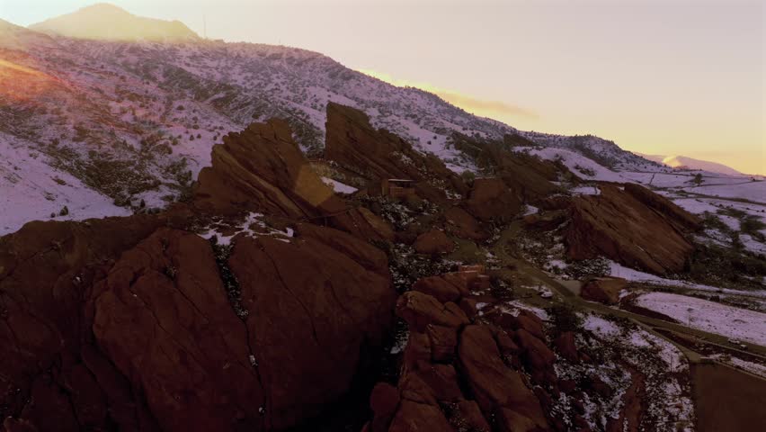 Snow-covered sunset over Red Rocks Park and Amphitheater music concert venue landmark Morrison Colorado aerial drone golden hour jagged Red Rocks Mt Morrison landscape Denver Front Range forward pan