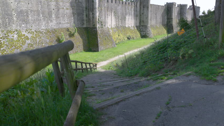 Imposing ancient stone fortress wall featuring fortification towers and a grassy defensive moat on a sunny day.