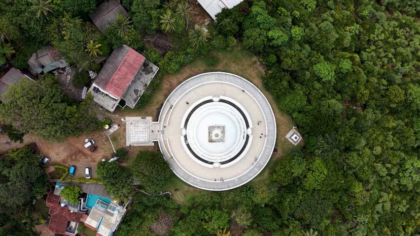 Aerial view of the Japanese Peace Pagoda - Rumassala surrounded by lush tropical forest and nearby buildings in Unawatuna, Southern Province, Sri Lanka.
