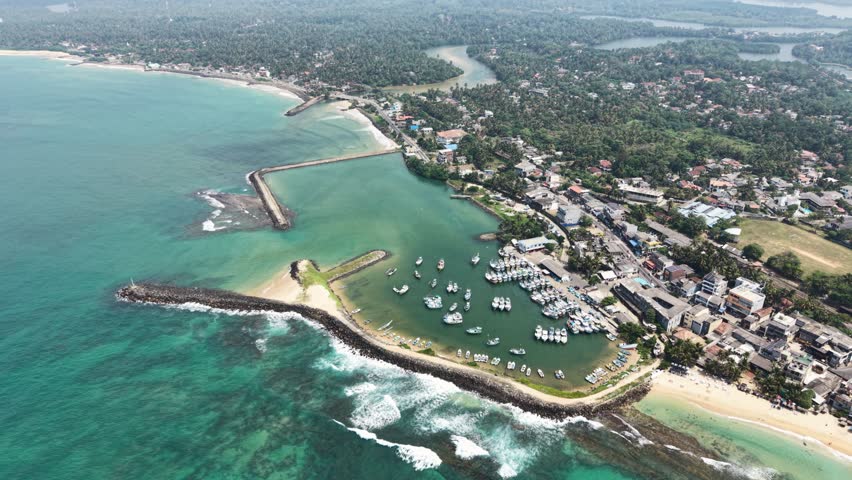 Aerial view of fishing boats docked in a harbor protected by breakwaters along the coastline of Hikkaduwa, Southern Province, Sri Lanka.