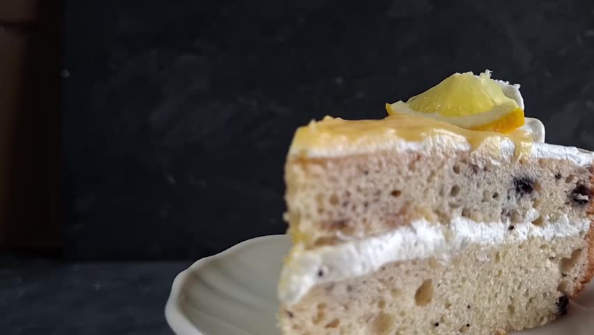 A Delicious Slice of Lemon Blueberry Cake with Whipped Cream Frosting Between Layers Spinning on a White Plate