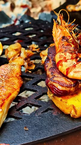 Fresh fish, prawns, and oysters grilling on a cast iron barbecue over hot charcoal embers