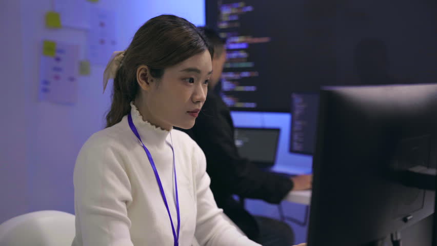 Young Asian woman and Caucasian man collaborating on robotic hardware device. Tech developers examining electronic components in modern laboratory with blue ambient lighting.