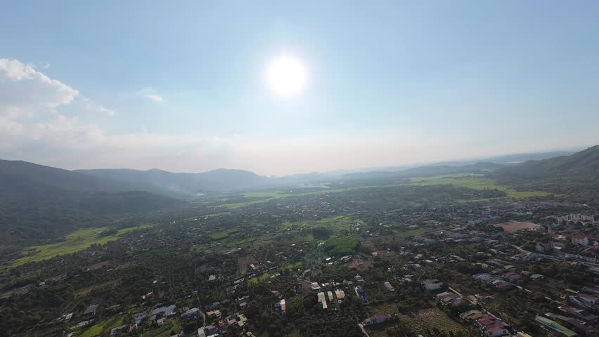 Beautiful aerial view facing the bright sun over rural fields and houses with a majestic mountain horizon.