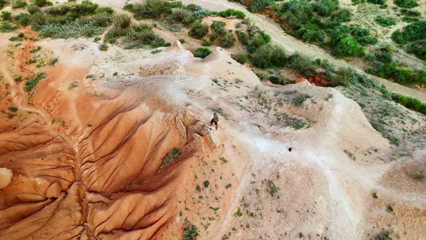 Aerial view of Skazka Canyon with its unique red sandstone formations and a person standing on a ridge Tosor, Issyk-Kul Region, Kyrgyzstan.