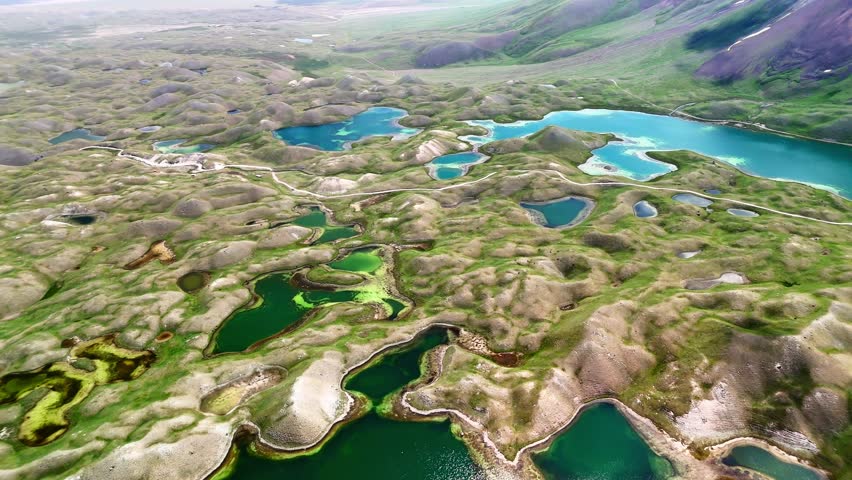 Aerial view of Tulpar Lake and numerous turquoise ponds scattered across the rolling green hills of the Alay District, Osh Region, Kyrgyzstan.