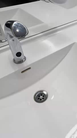 Close-up of a chrome automatic faucet over a white bathroom sink, with modern basin, drain, overflow slot, and clean public restroom design.
