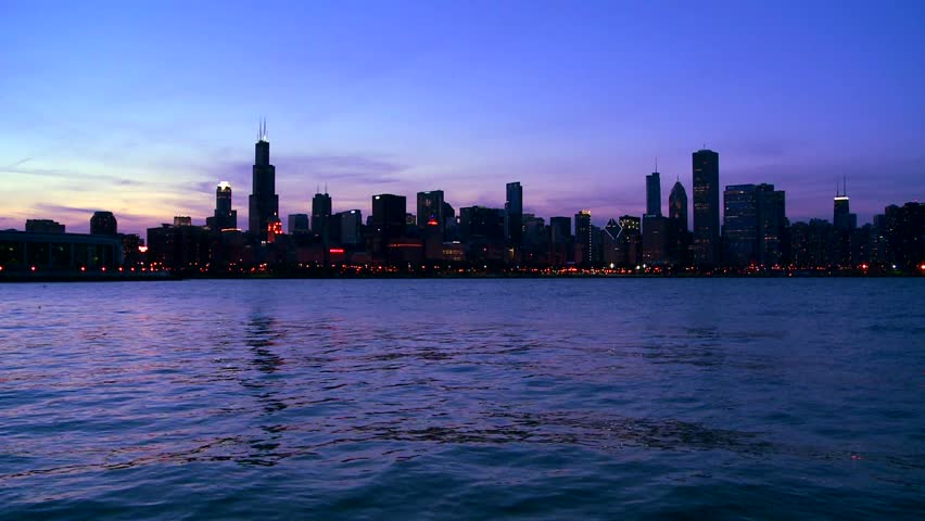 Panoramic view of chicago cityscape at twilight featuring iconic skyscrapers. Beautiful purple sunset sky glows over urban buildings. Gentle waves ripple in harbor during scenic evening shot.