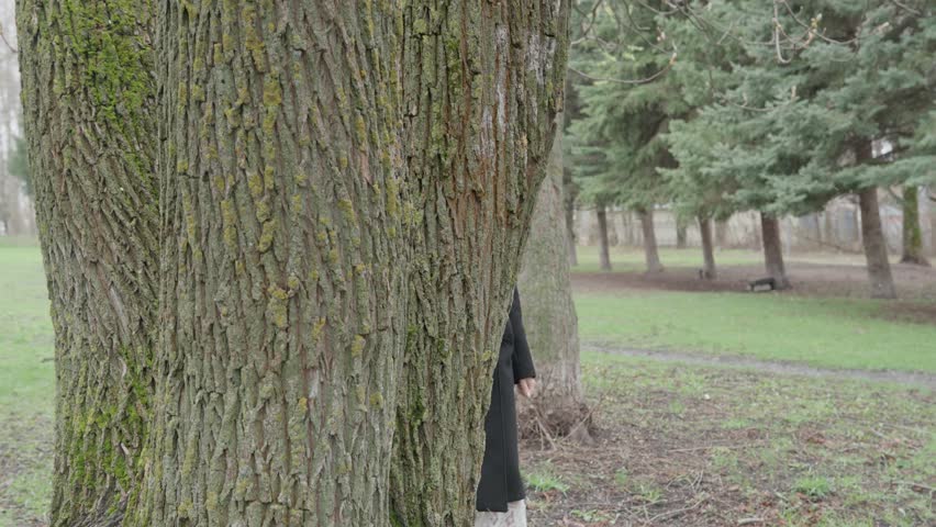 Young attractive woman walking in park among trees in black coat