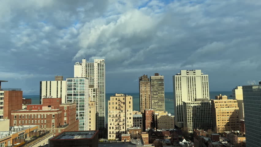 People see a skyline with tall buildings and clouds above. Lake Michigan is visible in the distance on a clear day.