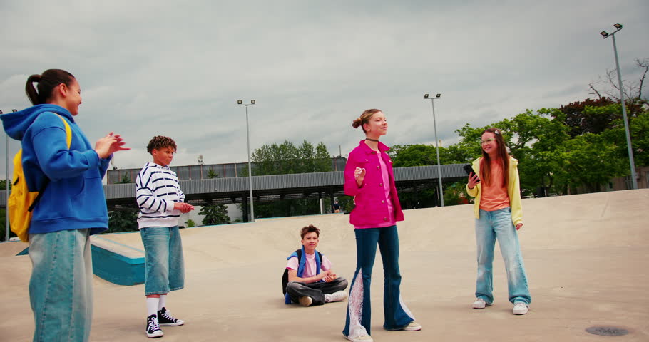 Group of stylish teenagers having fun together at an outdoor skatepark. Friends recording a viral dance video for social media on a smartphone