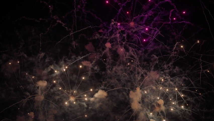 Stunning fireworks explosion fills the dark night sky over Dubai with brilliant golden sparks and vibrant purple hues. Smoke trails create dramatic patterns as pyrotechnics burst in celebration.